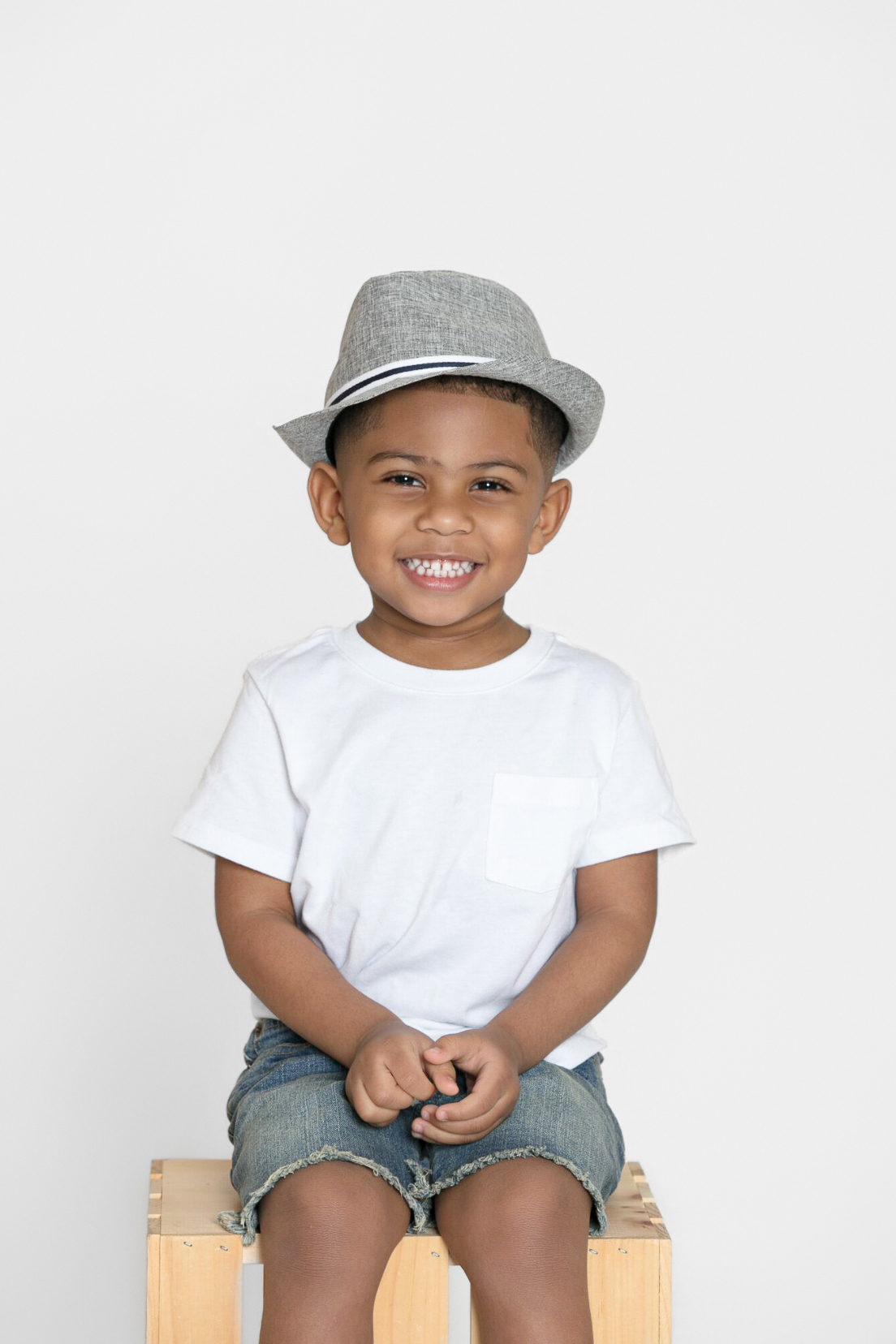 Smiling boy in a gray hat seated on a wooden crate